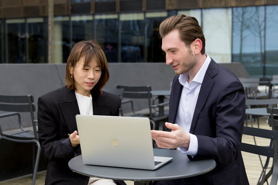 Two professionals collaborating over a laptop during an outdoor business meeting.