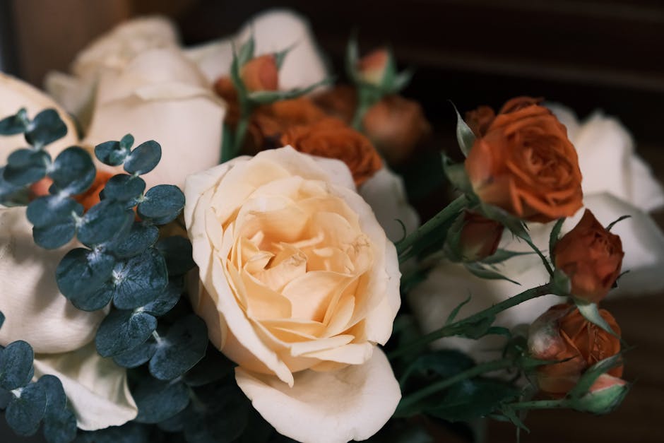 A close-up shot of a bouquet featuring white and orange roses with eucalyptus leaves.