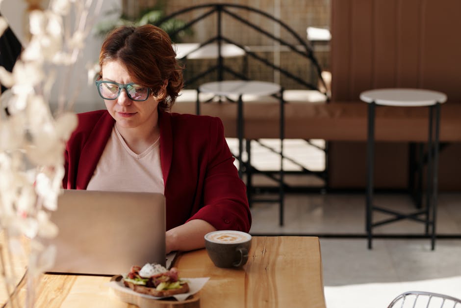 Professional woman in café using laptop while enjoying coffee, symbolizing remote work lifestyle.