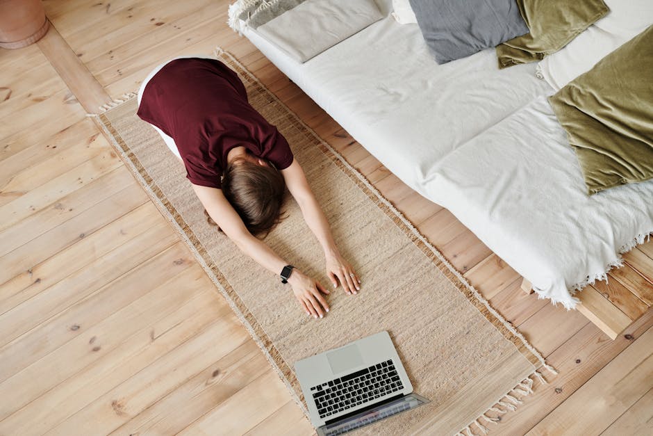 Woman in yoga pose on mat, indoors with laptop, showing mindfulness and home fitness.