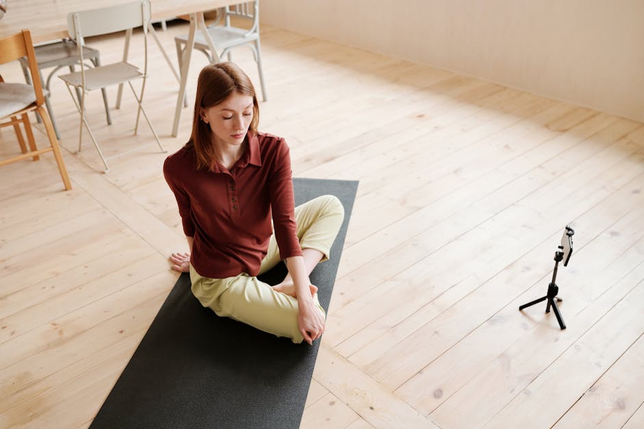 Young woman practicing yoga indoors with smartphone setup for recording, demonstrating flexibility and mindfulness.