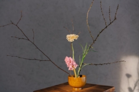 A minimalist floral arrangement in a wooden vase with branches and soft lighting.