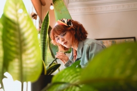 A red-haired woman tending to houseplants with natural light indoors.