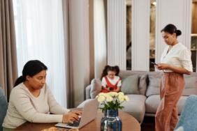 A woman works on a laptop while others use devices in a cozy living room setting.